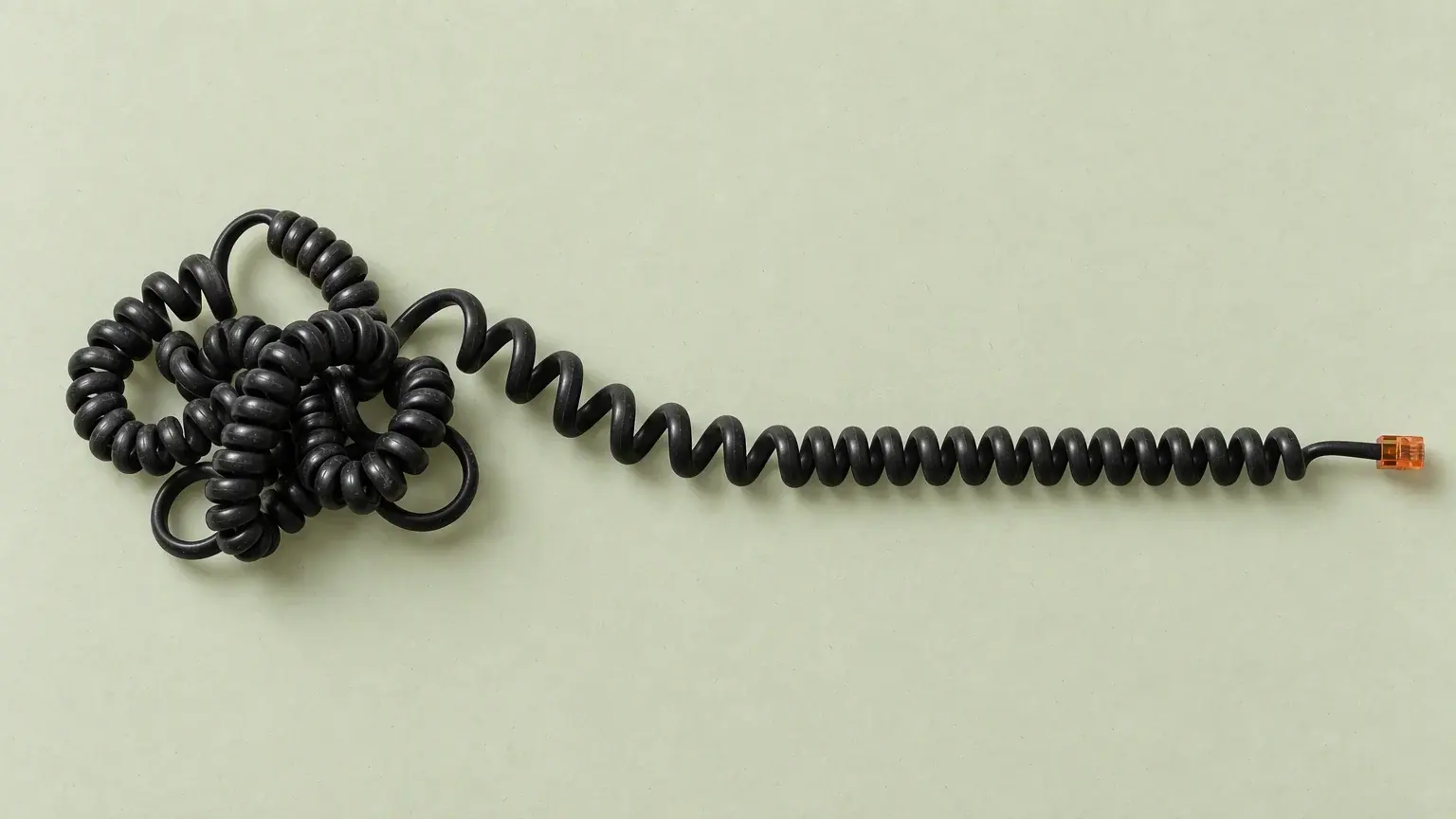 A coiled telephone handset cord photographed from above, knotted into a tangle at one end and running out straight to its plug at the other