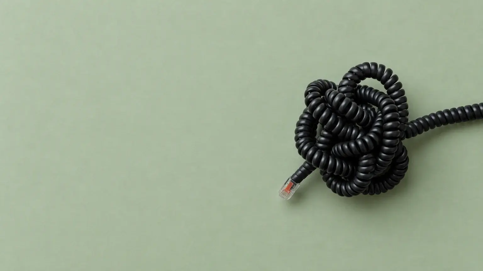 A coiled telephone cord photographed from above on sage paper, knotted into a tangle with one strand running away