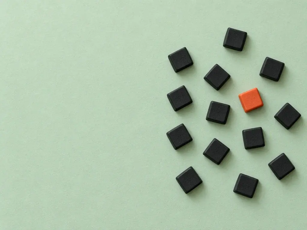 Blank black keypad buttons scattered loose on mint paper, one of them orange