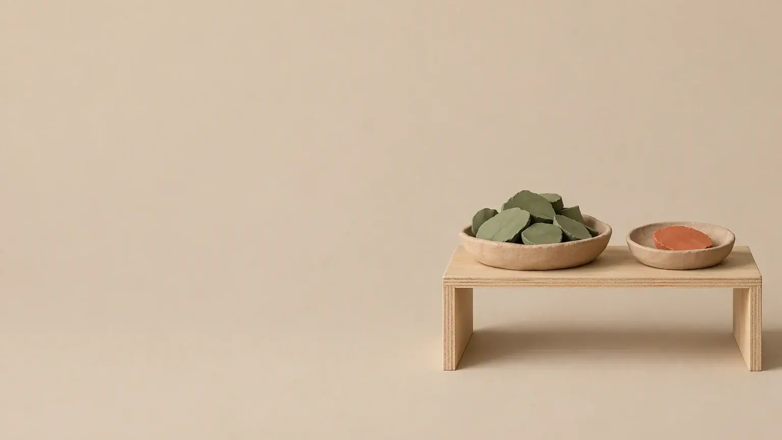 A low plywood shelf holding two shallow clay sorting trays, one stacked deep with green slips and one holding a single orange slip